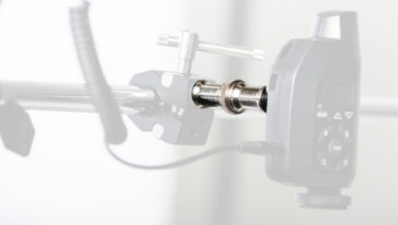 Close-up of a metal clamp holding a cylindrical shaft connected to a black electronic control unit with a display and buttons in a workshop setup.