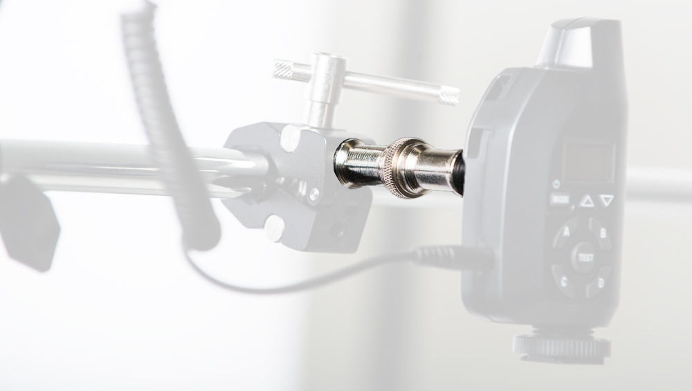 Close-up of a metal clamp holding a cylindrical shaft connected to a black electronic control unit with a display and buttons in a workshop setup.