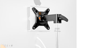 Wall-mounted monitor arm attached to the back of a white display with a visible Tether Tools mounting plate.