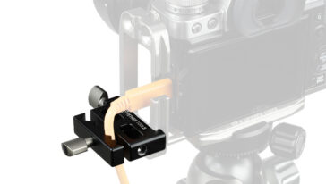 Close-up of a black camera cable clamp securing an orange cable to a camera rig on a tripod head.