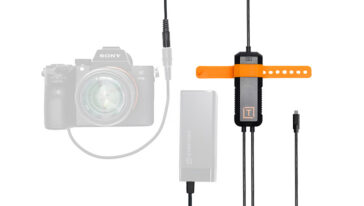 DSLR camera connected by a cable to an external battery pack and an orange mounting tether device on a stand