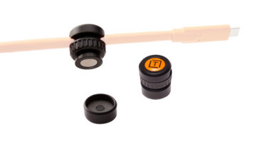 Set of three black caps with one orange top cap bearing a logo, arranged near a beige rod on a white background