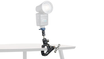 Westcott FJ80 studio flash mounted on a desk-edge clamp with an adjustable arm over a table surface, light head pointing upward.