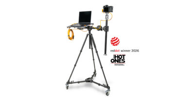 Camera rig on a wheeled tripod with a laptop and camera mounted on a vertical arm; orange cables extend from the setup, with red dot winner 2026 and HOT ONES logos nearby.