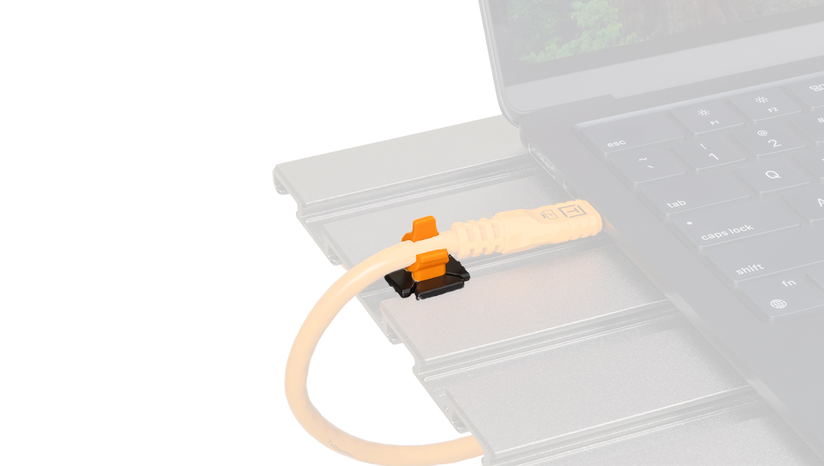 Close-up of an orange Ethernet-like cable plugged into a slim, silver docking module beside a laptop keyboard.