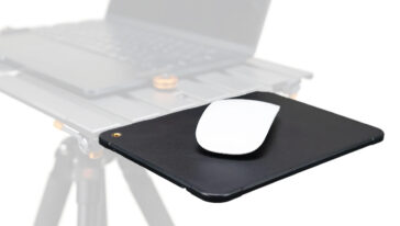 White wireless mouse resting on a black mousepad with a laptop blurred in the background, suggesting a desk setup for computing.