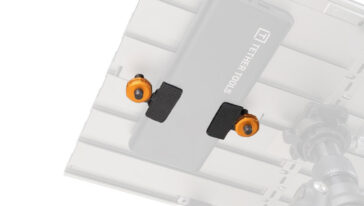 Close-up of a gray camera mounting plate with two black clamp pads and orange thumbscrews on a metal rig.