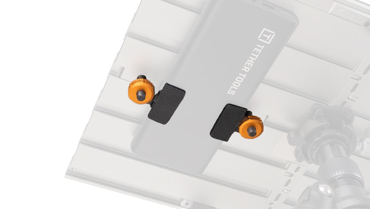 Close-up of a gray camera mounting plate with two black clamp pads and orange thumbscrews on a metal rig.