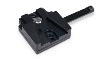 Black metal quick-release clamp with adjustable jaws and a long lever, used to secure parts in a jig or fixture in a workshop.
