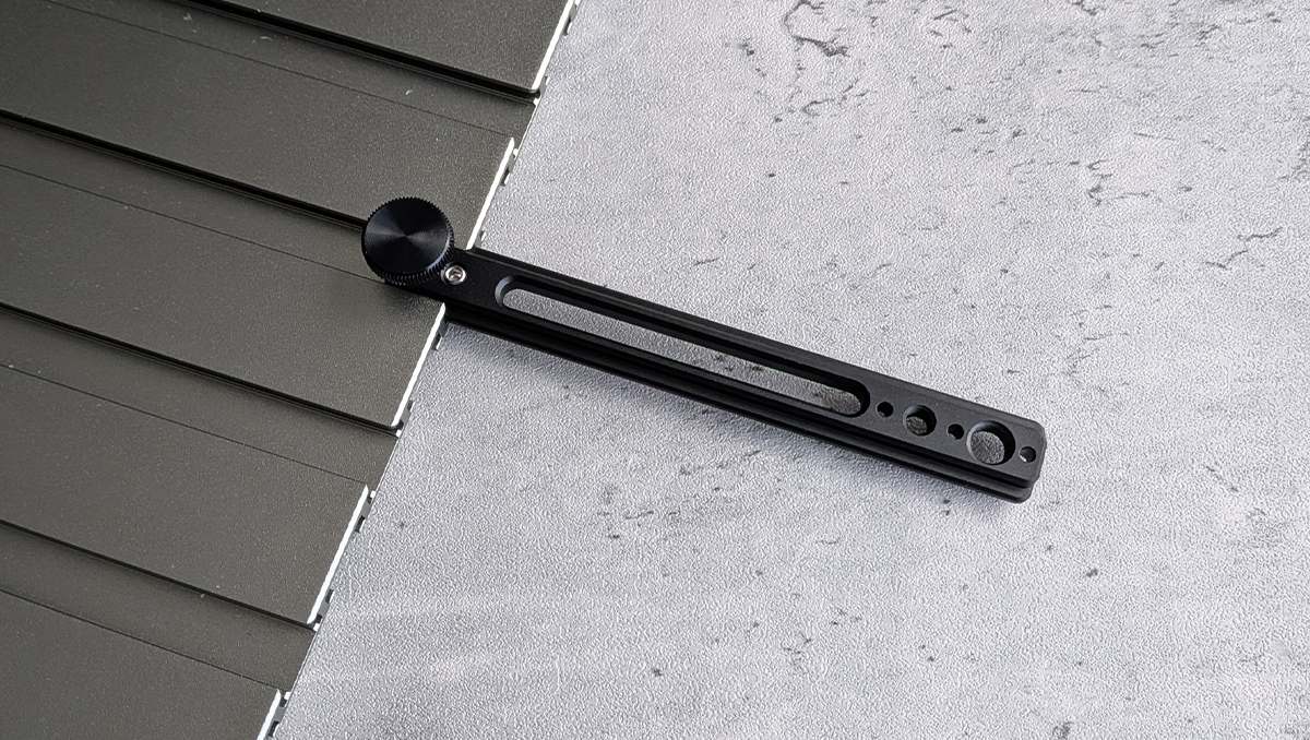 Black adjustable mounting rail with a circular knurled knob resting on dark rooftop panels; used to secure components to a surface.