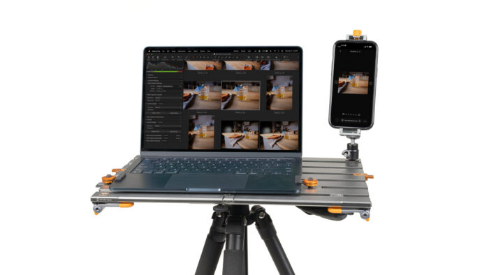 Portable editing rig: laptop on a metal platform with a smartphone mounted on the side, displaying photo thumbnails on both screens.