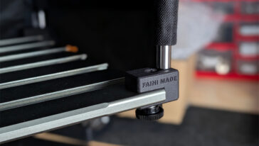 Close-up of a 3D printer bed clamp with a black textured knob securing the bed rail.