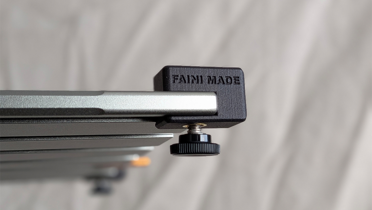 Close-up of a metal camera slider rail with a black end block and a knurled adjustment knob.