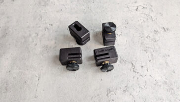 Four small black clamping blocks with adjustment knobs spread on a gray textured surface