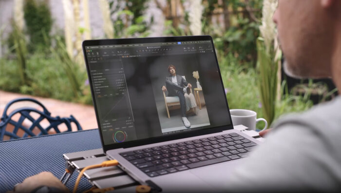 Person editing a portrait on a laptop outdoors, the screen showing a man seated in a chair model.