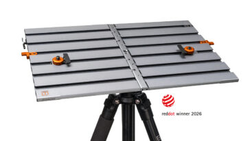 Adjustable metal work table on a tripod with orange clamps; Red Dot Winner 2026 badge nearby.