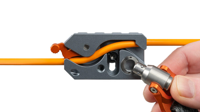 Close-up of a hand operating a precision wire stripper/crimping tool on an orange electrical wire to strip insulation or crimp a connector.