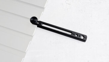 Close-up of a black metal blind tilt rod with a round knob resting against white window blinds on a light surface, showing the adjustment hardware.