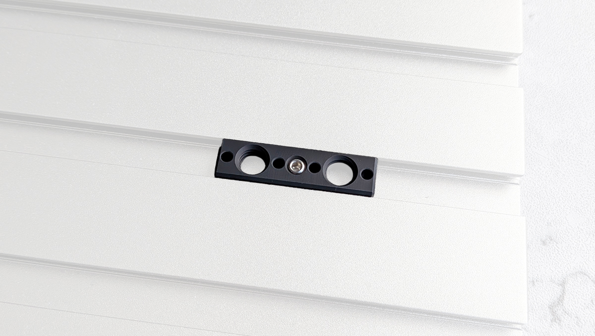 Close-up of a black mounting bracket with two circular holes and a central screw on white wall panels.
