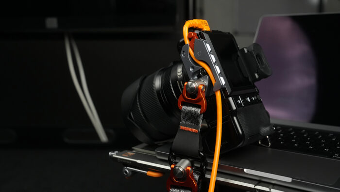 Close-up of a DSLR camera mounted on a metal rig with orange cables and clamps, resting on a laptop.
