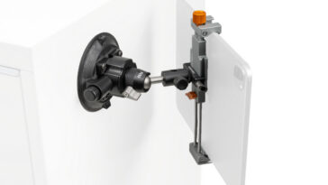Precision alignment device mounted on a white cabinet, featuring a black dial, silver rod, and orange adjustment knob.