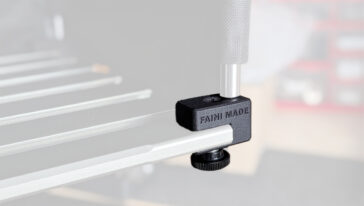 Close-up of a black clamping accessory attached to a silver aluminum rail, securing a workpiece in a workshop setup