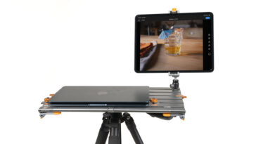 Portable camera rig with a laptop on a metal rail platform and a mounted tablet displaying a photo of a glass of whiskey on the table on screen.