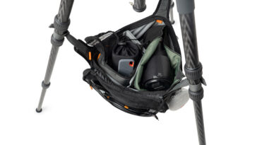 Open camera bag attached to a tripod, revealing a camera body, lens, and accessories inside.