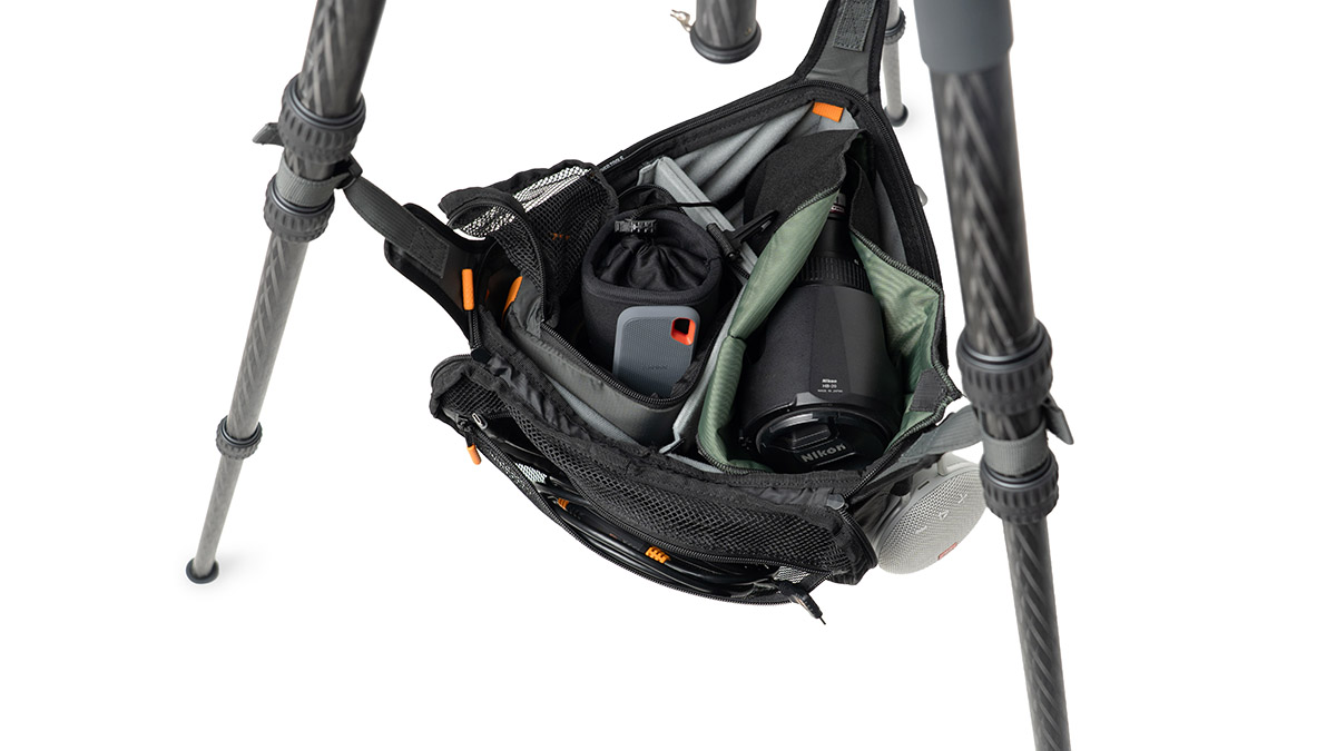 Open camera bag attached to a tripod, revealing a camera body, lens, and accessories inside.